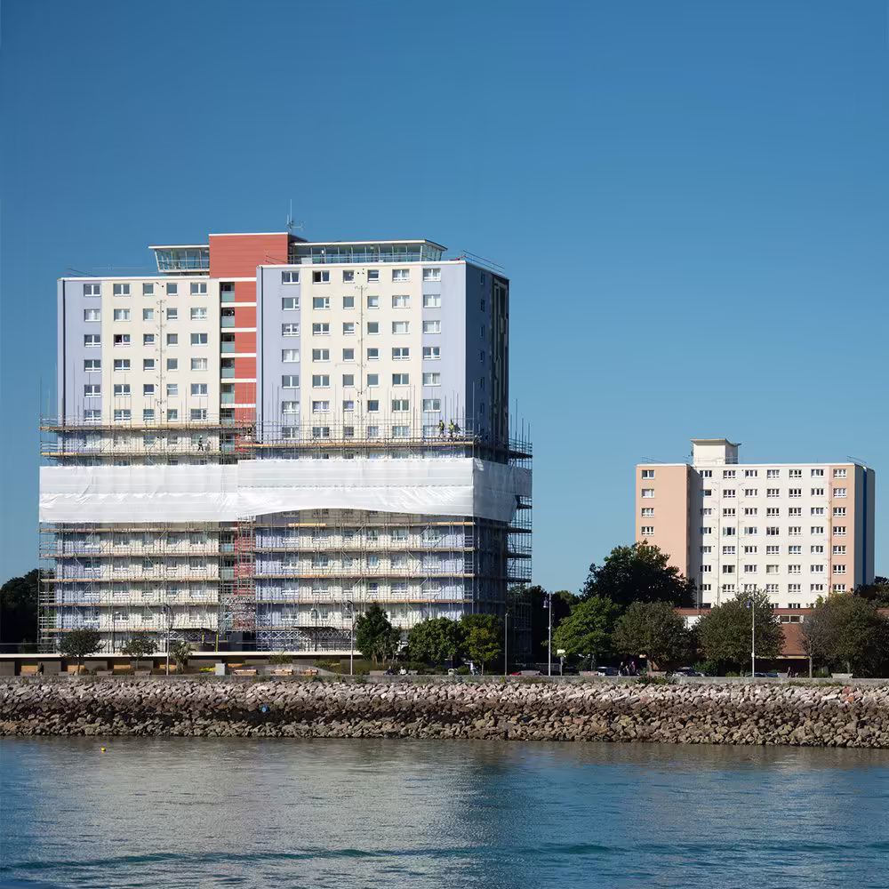 A view from the sea of a Gosport tower block mid-way through its cladding replacement, with the upper floors completed and the lower floors still covered in scaffolding.