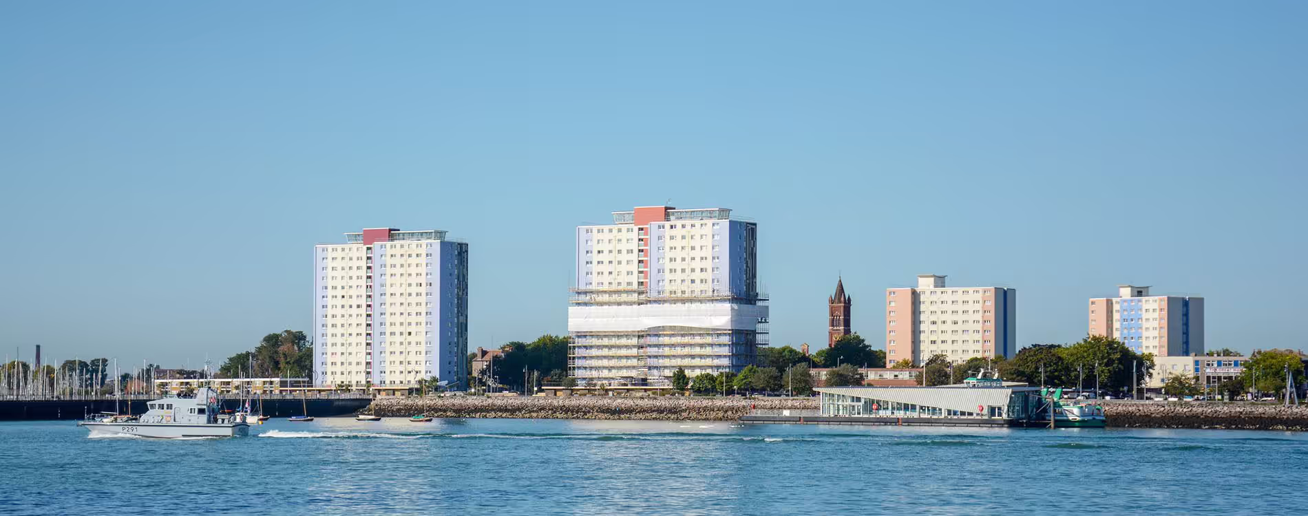 A panoramic view from the water of the Gosport Towers on the waterfront, with one high-rise block undergoing cladding replacement works with visible scaffolding.