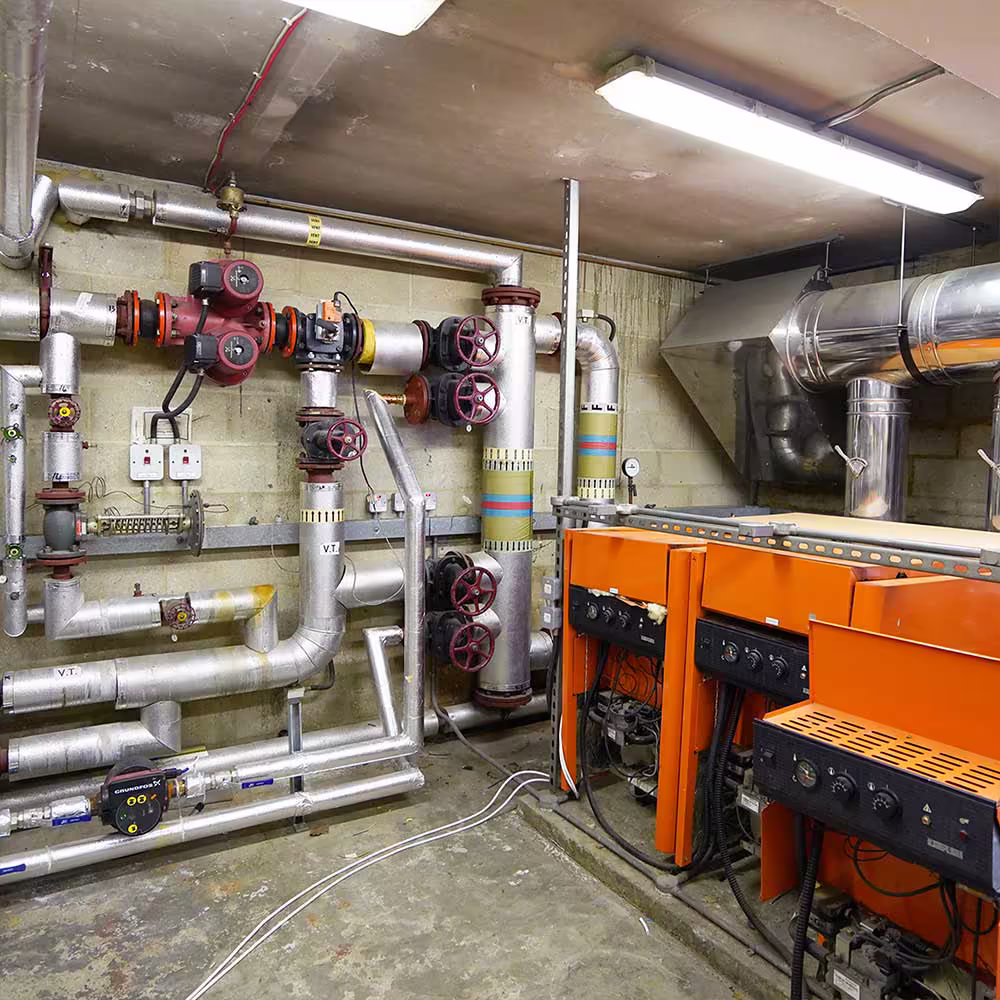 The old communal heating system, highlighting the outdated orange boilers and the complex, poorly insulated pipework before the replacement project.