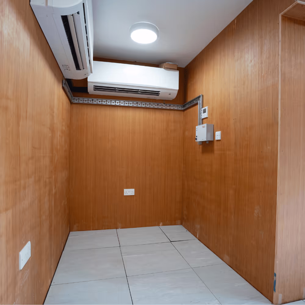 The interior of a small, modernised room within the heritage building, showing new air conditioning units, a tiled floor, and wood-panelled walls.