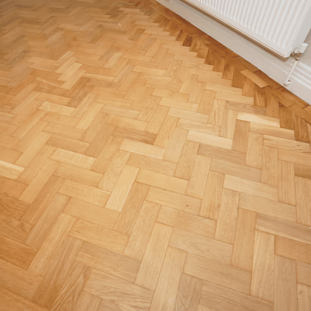 A close-up of a newly installed solid oak herringbone parquet floor, showcasing the high-quality finish and warm tones of the wood in a refurbished office space.
