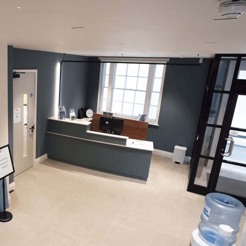 The newly refurbished office reception area, featuring a modern grey desk with a privacy screen, a large sash window, and clean, contemporary tiling.