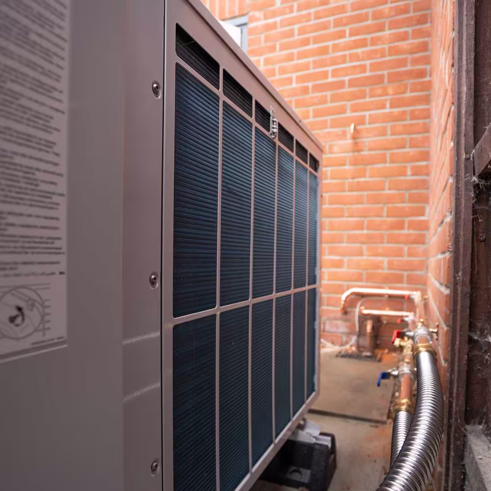 The rear of an Air Source Heat Pump outdoor unit, showing the heat exchanger fins and the connection of the flow and return pipework.