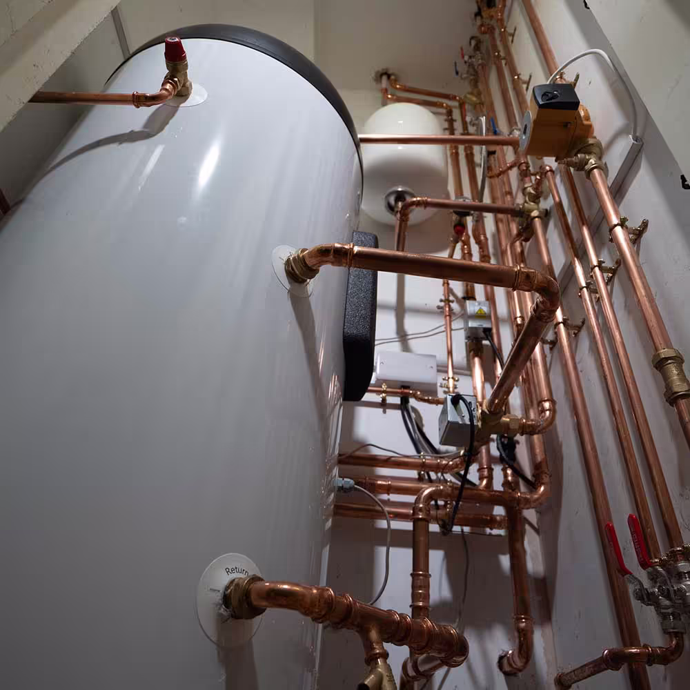 The complex and neatly installed internal pipework for a residential ASHP system, showing the hot water cylinder, expansion vessel, pump, and copper pipes.